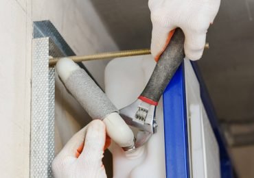 A worker is using a spanner wrench to connect the pipe to the built-in tank of the suspended toilet. Top view